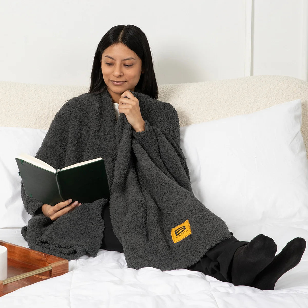 Woman wrapped in charcoal gray oversized blanket reading on bed