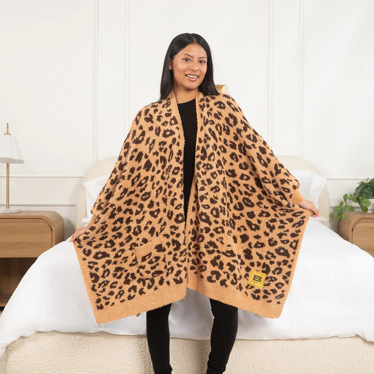 Woman wearing tan leopard print oversized blanket wrap on bed in modern bedroom