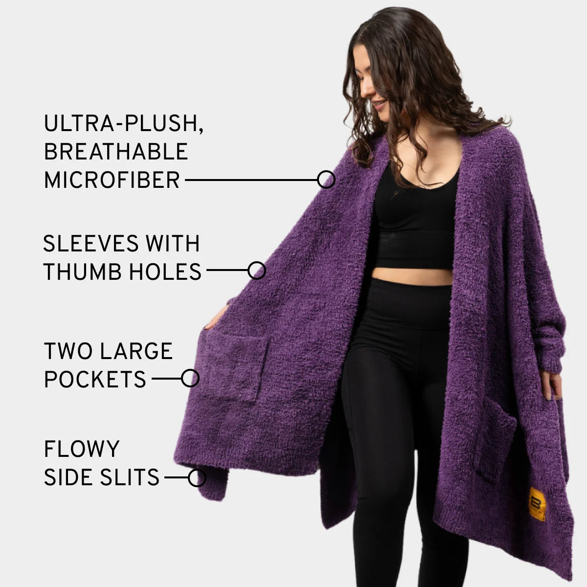 Woman wearing deep purple oversized plush wrap blanket with thumb holes, pockets, and side slits over black outfit