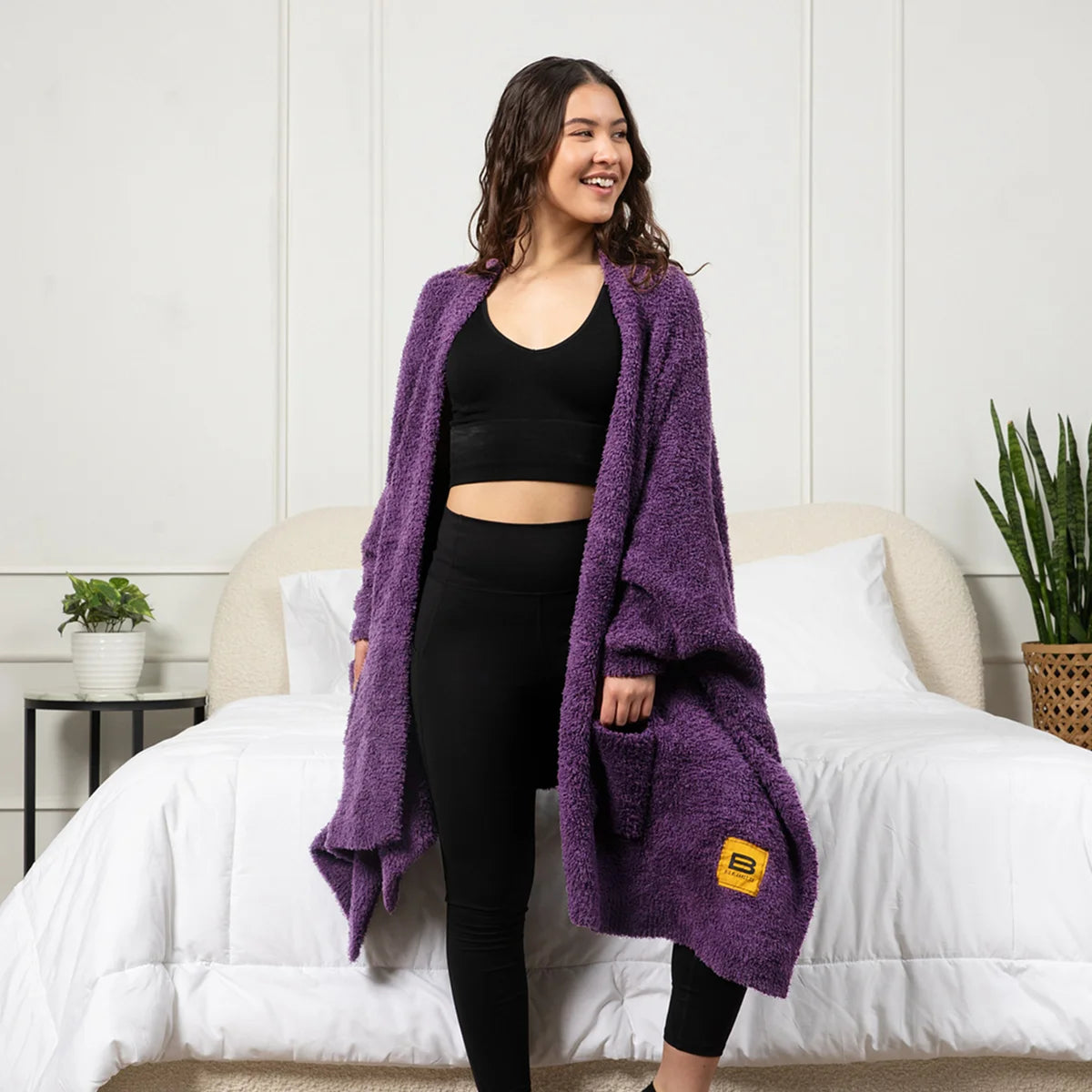 Woman wearing deep purple oversized blanket wrap draped over shoulders on bed