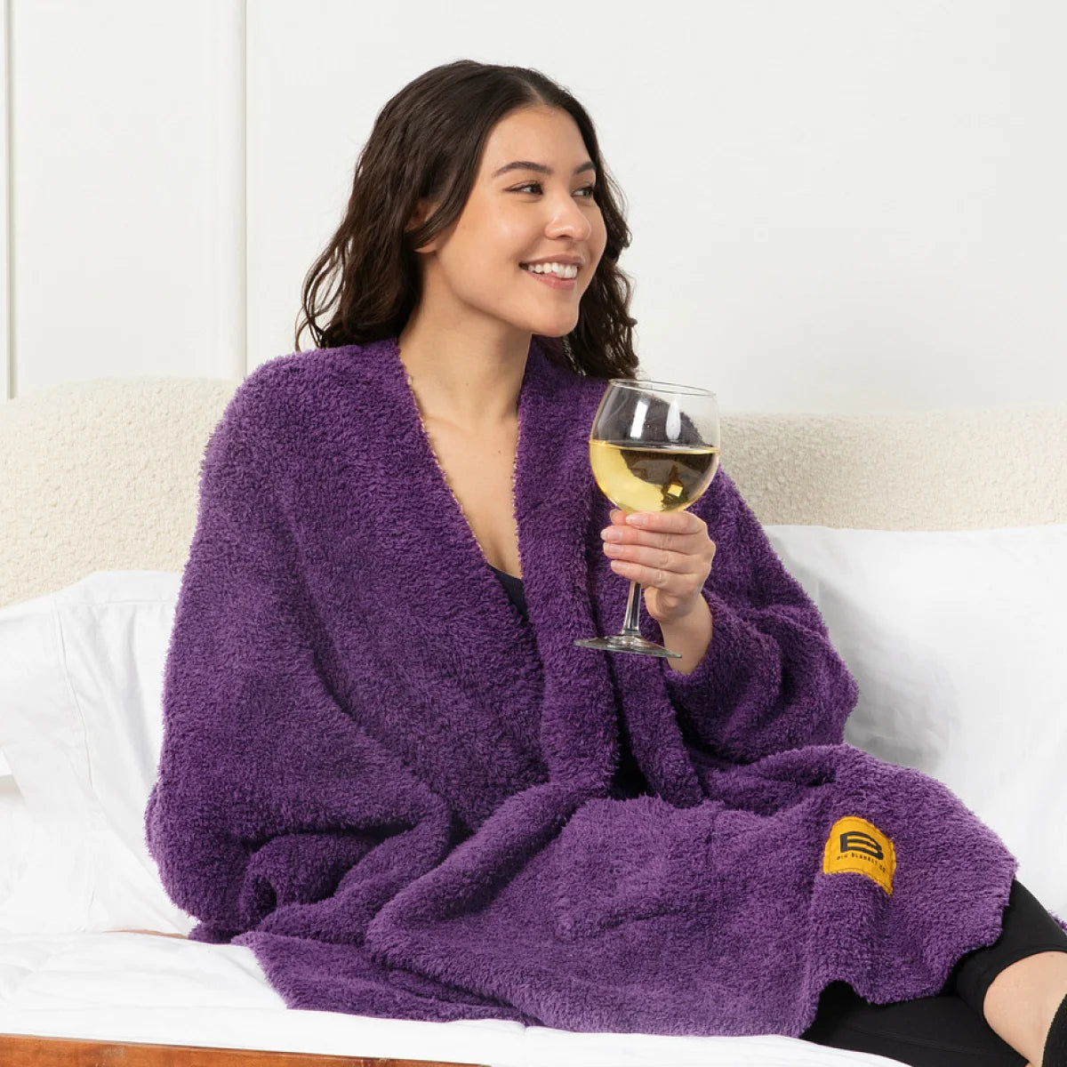 Woman wrapped in deep purple oversized fuzzy blanket sitting on couch holding wine glass