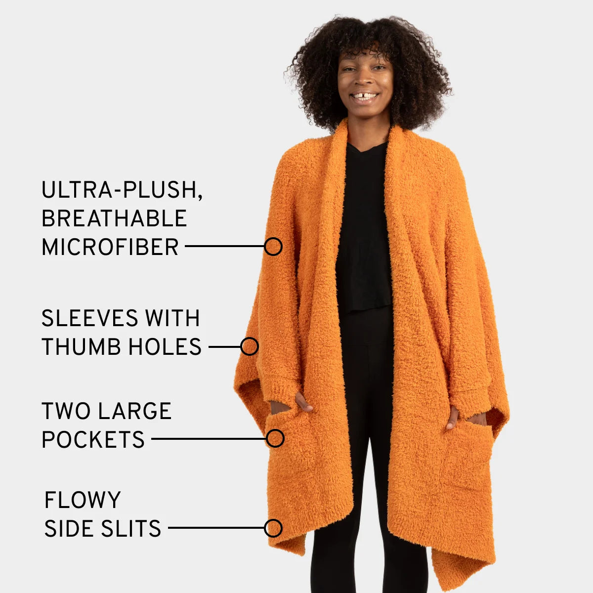 Woman wearing orange oversized Premier Plush wrap with thumb hole sleeves, deep pockets, and flowing side slits over black top