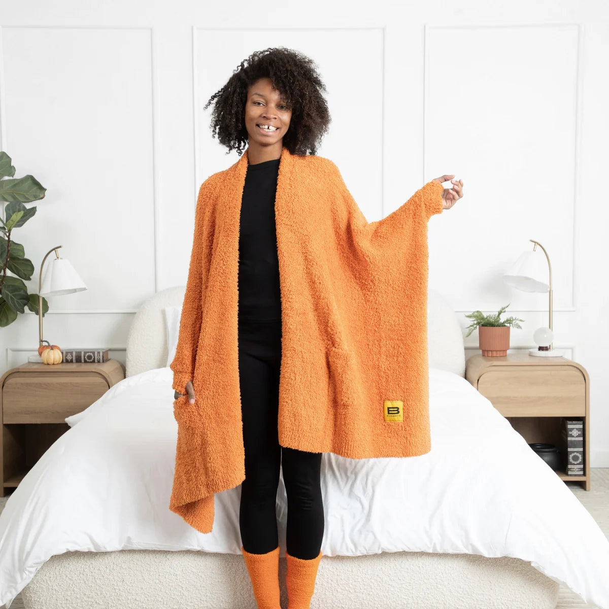 Woman wearing burnt orange oversized blanket wrap draped over shoulders on bed, demonstrating size and texture