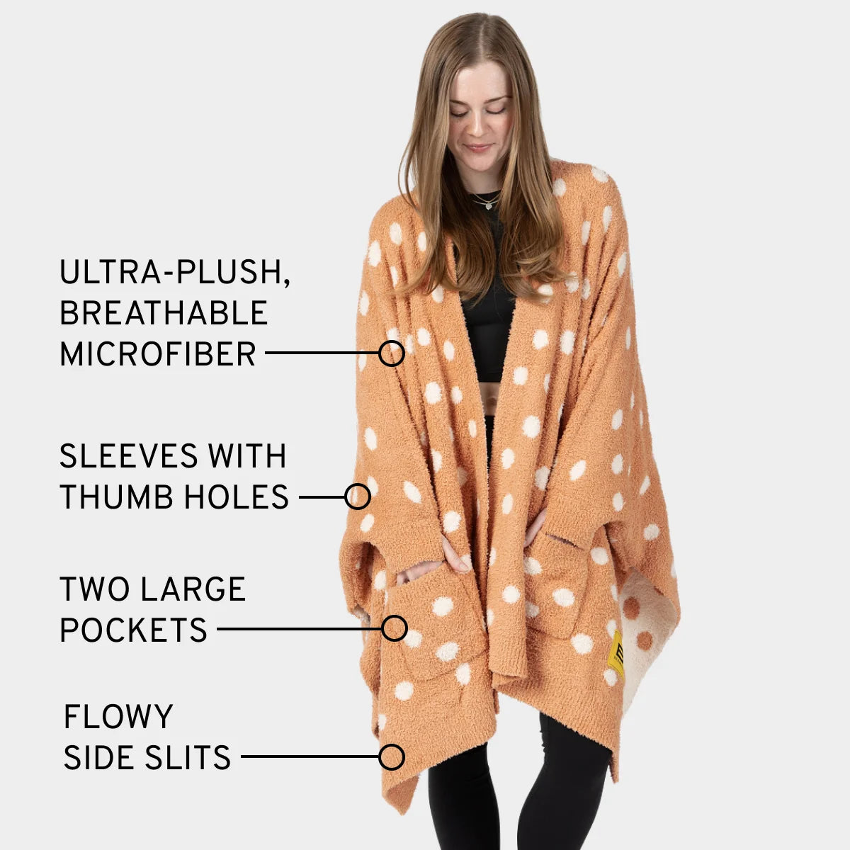 Woman wearing tan oversized blanket wrap with white polka dots, thumb holes, pockets, and side slits