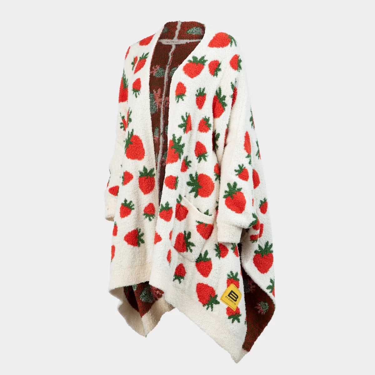 Oversized cream blanket with red strawberry and green leaf pattern, brown reverse side, draped over shoulders