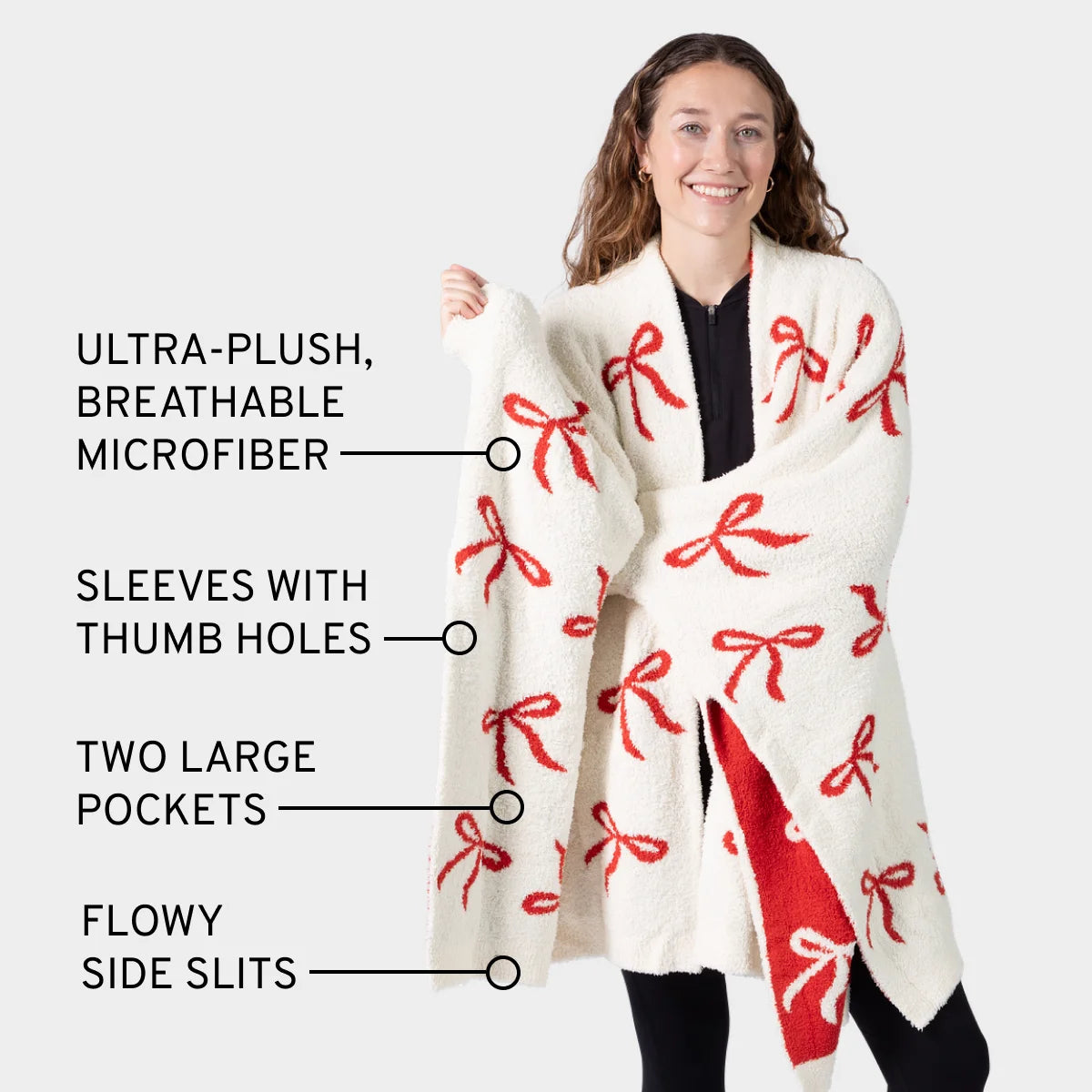 Cream oversized wrap with red bow pattern, thumb holes in sleeves, two large pockets, and side slits, worn by smiling woman