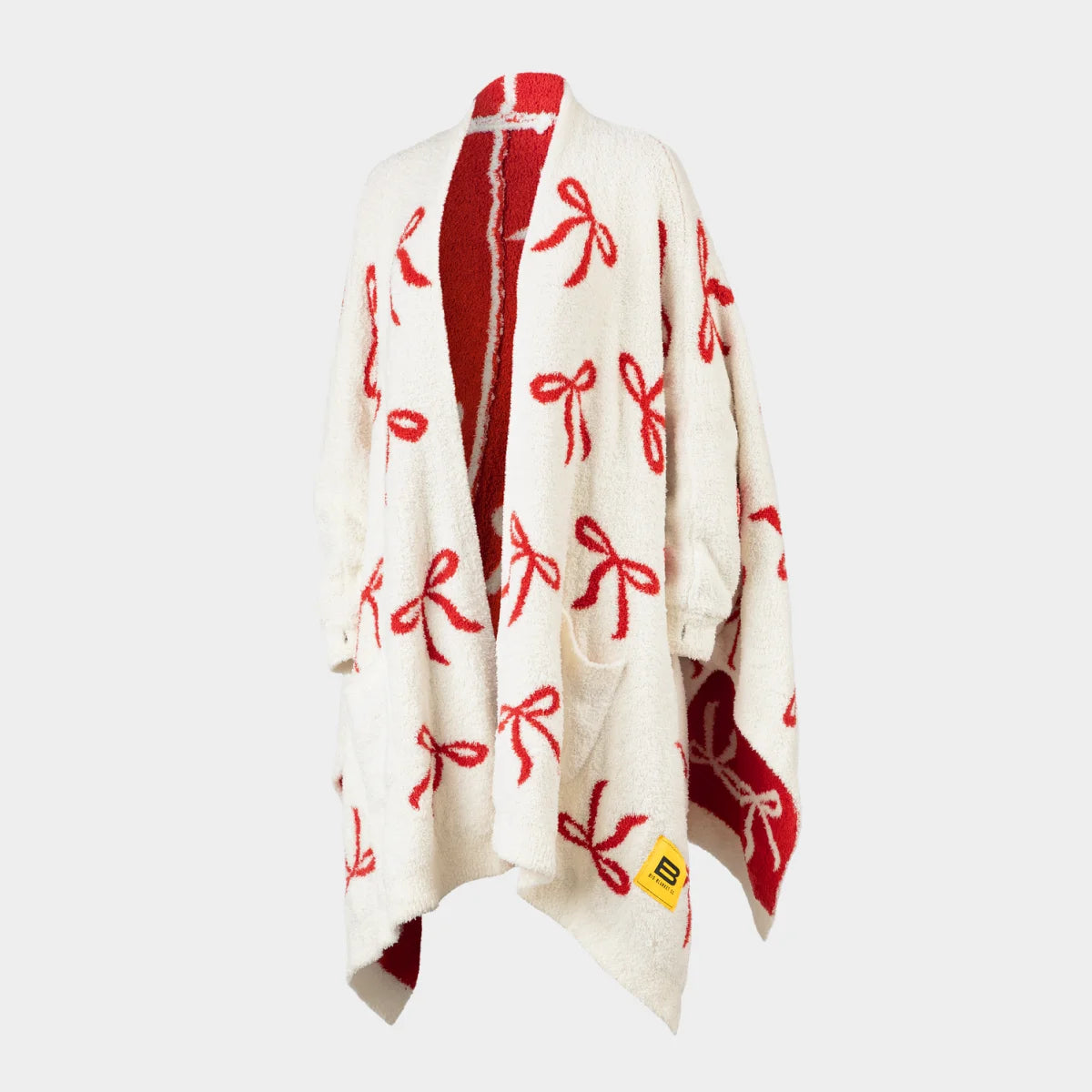 Cream oversized blanket wrap with red bow pattern throughout, red striped collar, and red reverse side, draped on shoulders