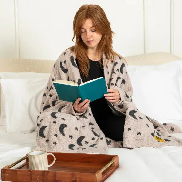 Woman reading on bed wrapped in oversized cream blanket with moon and star pattern