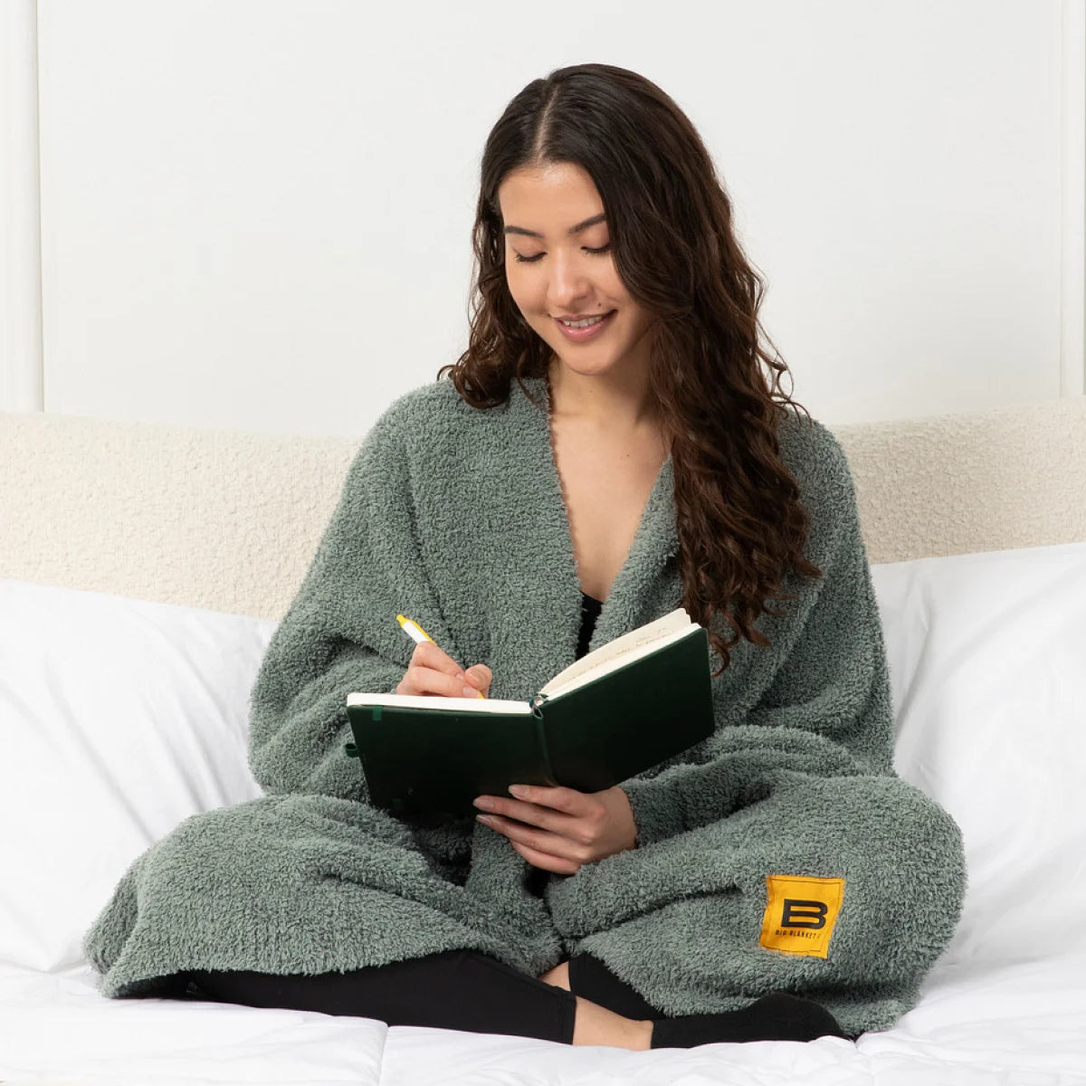 Woman wearing sage green oversized blanket wrap while reading on bed
