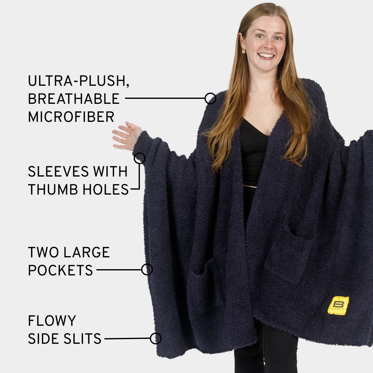 Woman wearing dark blue oversized wearable blanket with sleeves, thumb holes, pockets, and side slits