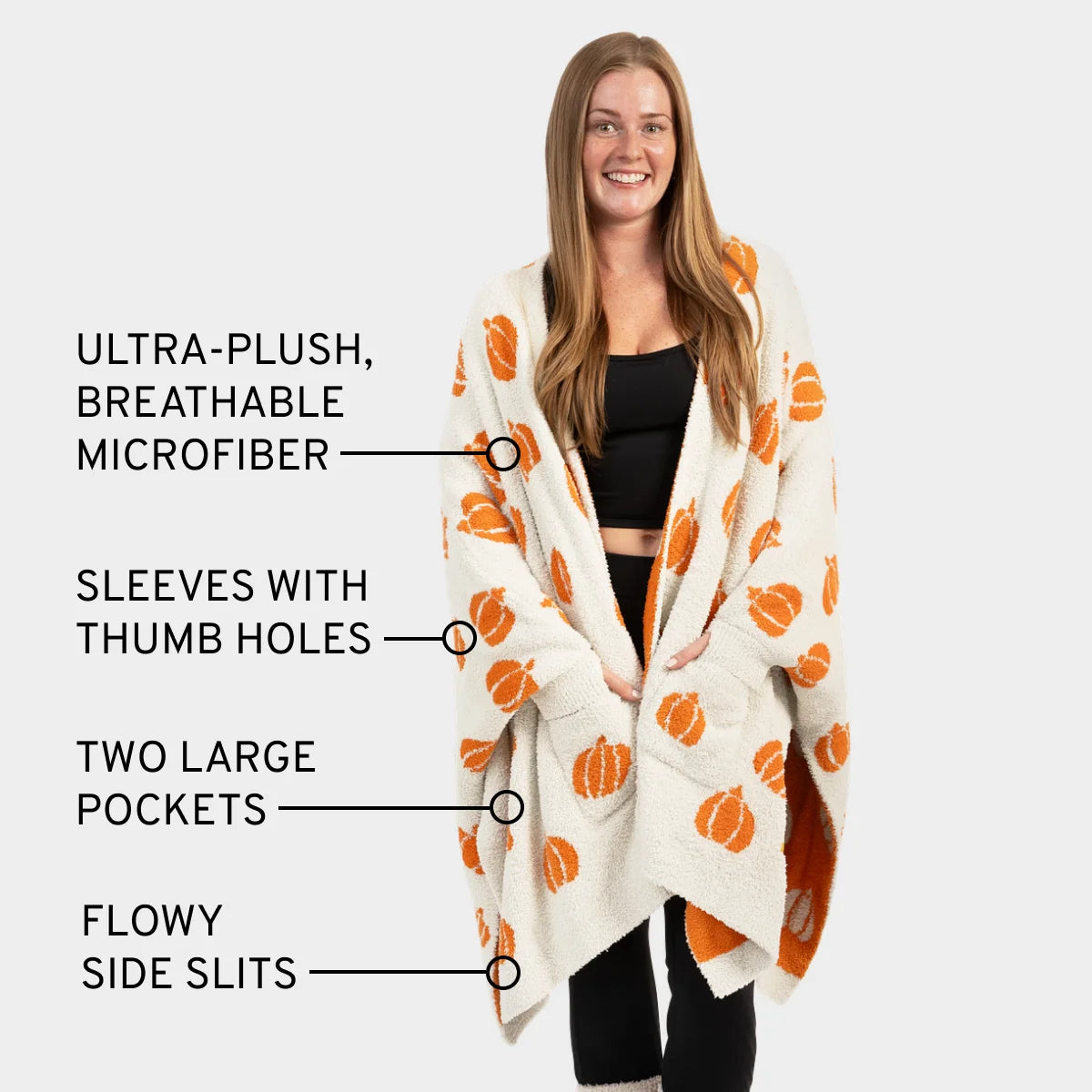 Woman wearing cream oversized blanket wrap with orange pumpkin pattern, thumb holes, pockets, and side slits