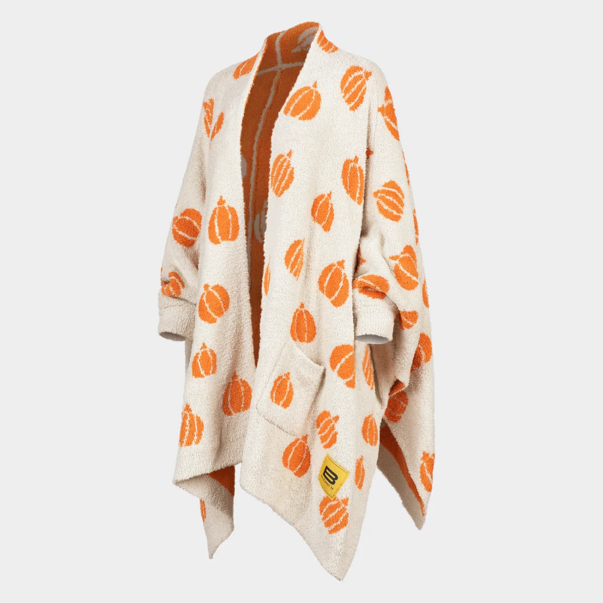 Cream oversized blanket wrap with orange pumpkin pattern and rust lining, draped on figure