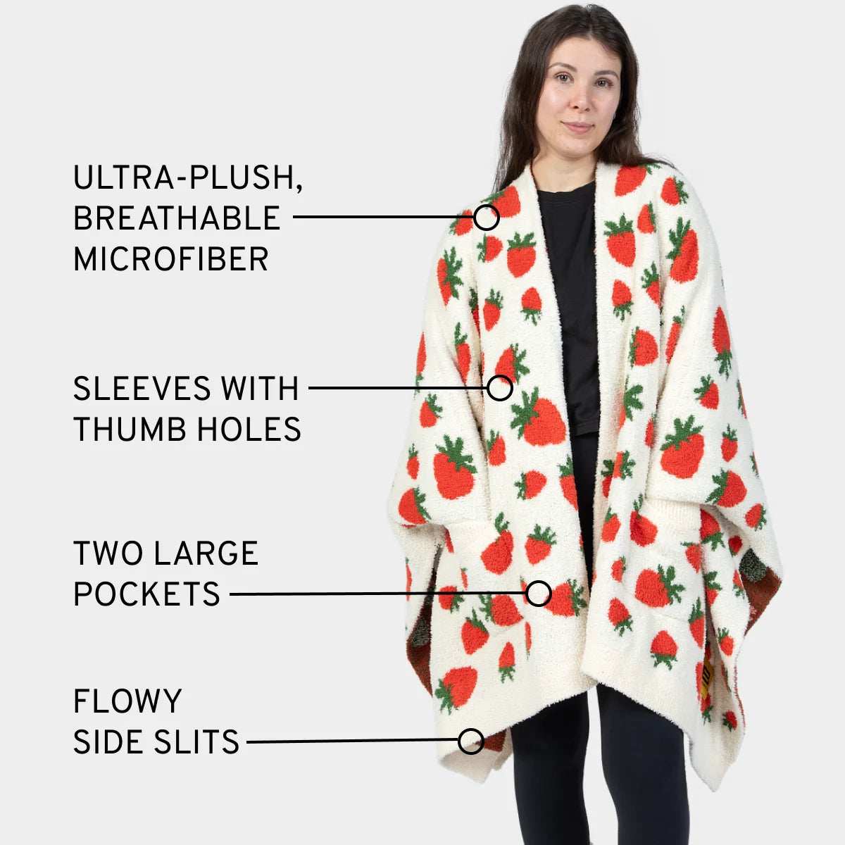 Woman wearing cream wearable blanket with red strawberry pattern, thumb holes, pockets, and side slits
