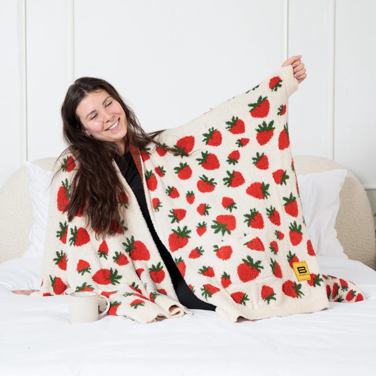 Cream oversized blanket with red strawberry and green leaf pattern, draped over woman on couch
