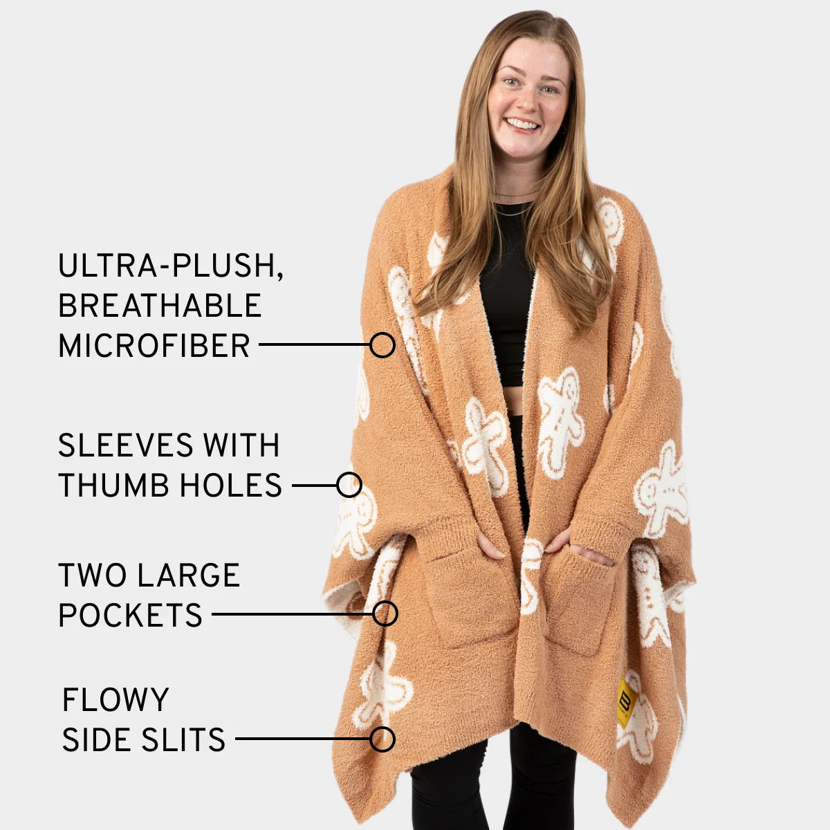 Tan oversized blanket wrap with white gingerbread pattern, thumb holes, large pockets, and side slits worn by smiling woman