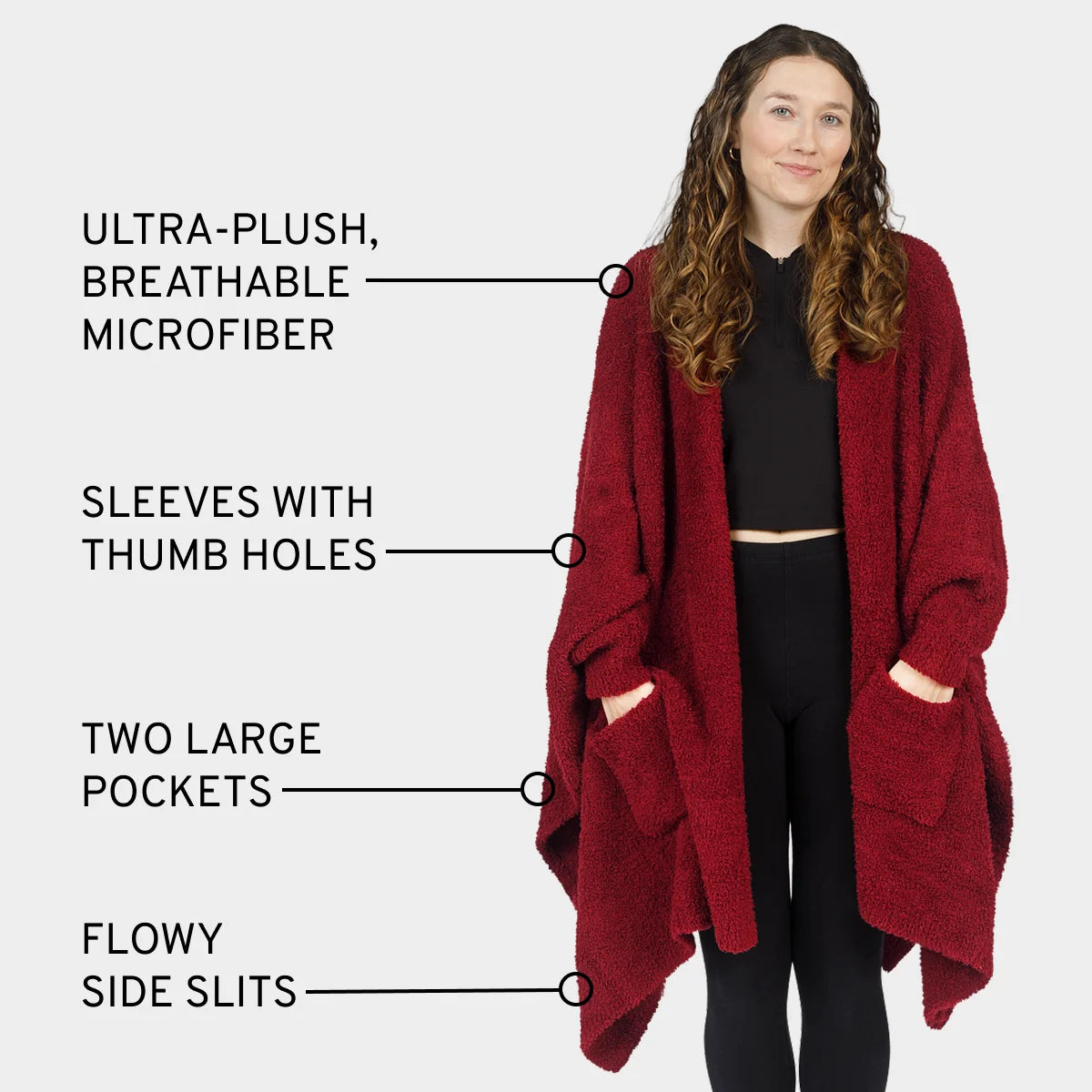 Woman wearing burgundy oversized blanket wrap with thumb hole sleeves, pockets, and side slits over black outfit