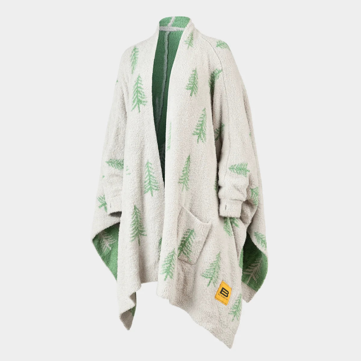 Cream oversized blanket wrap with green pine tree pattern, draped on shoulders showing texture and front pockets