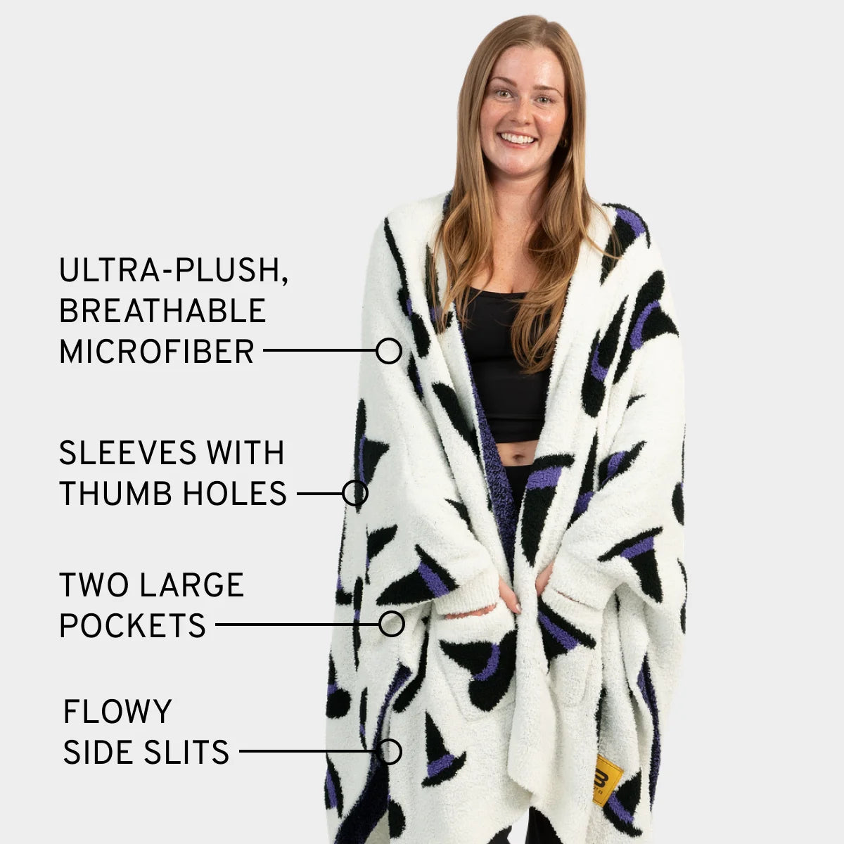 Woman wearing cream oversized blanket wrap with purple and black geometric pattern, thumb hole sleeves, large pockets, and side slits